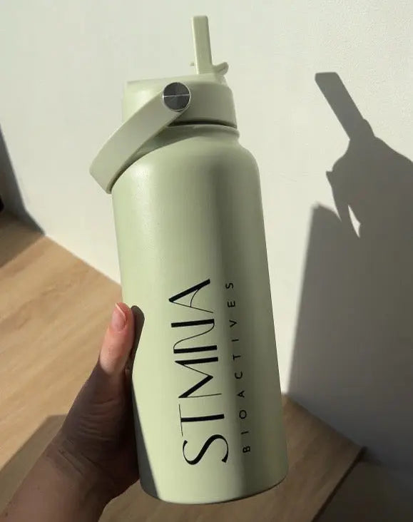 Light green water bottle with straw lid held by a hand on a wooden surface.