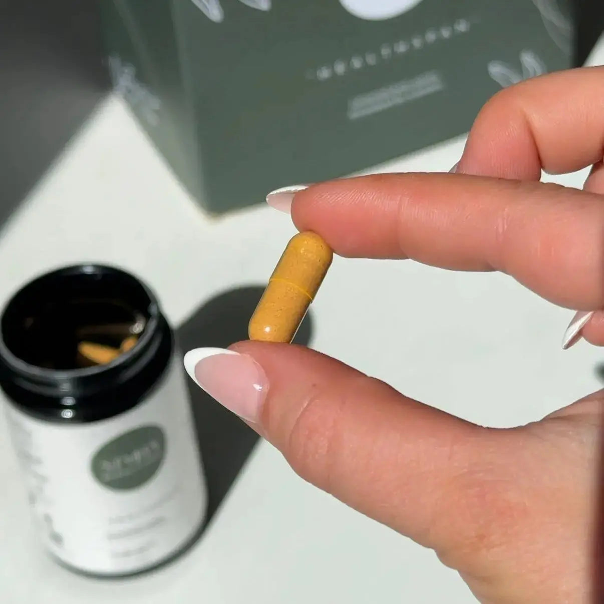 Hand holding an orange capsule product with a blurred background