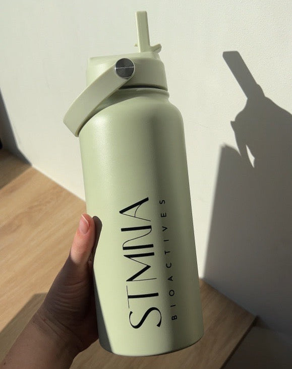 Light green water bottle with straw lid held by a hand on a wooden surface.