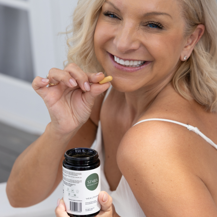 Woman holding a supplement capsule and bottle with a blurred background