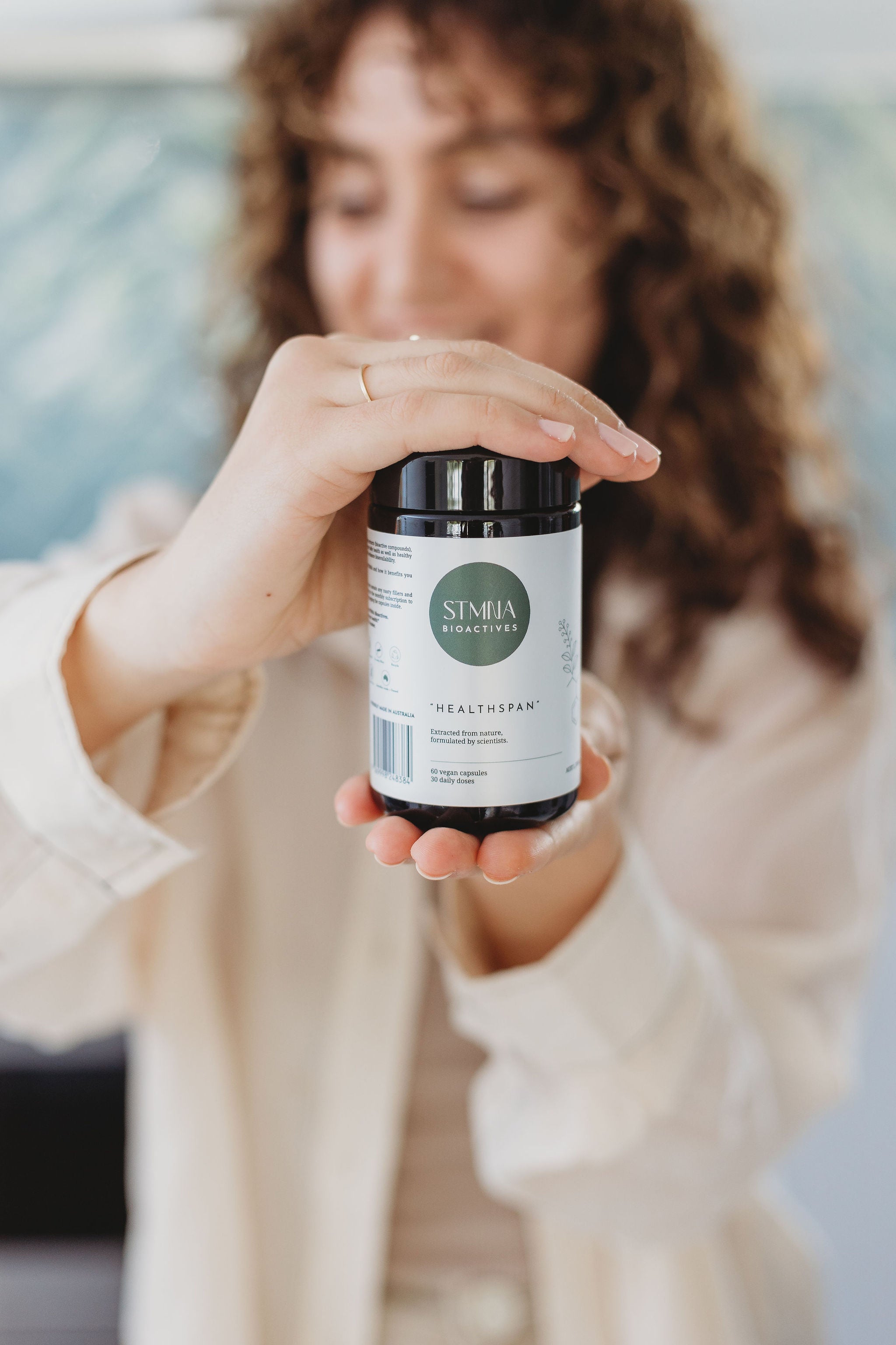 Person holding a supplement container with 'STMNA' branding.