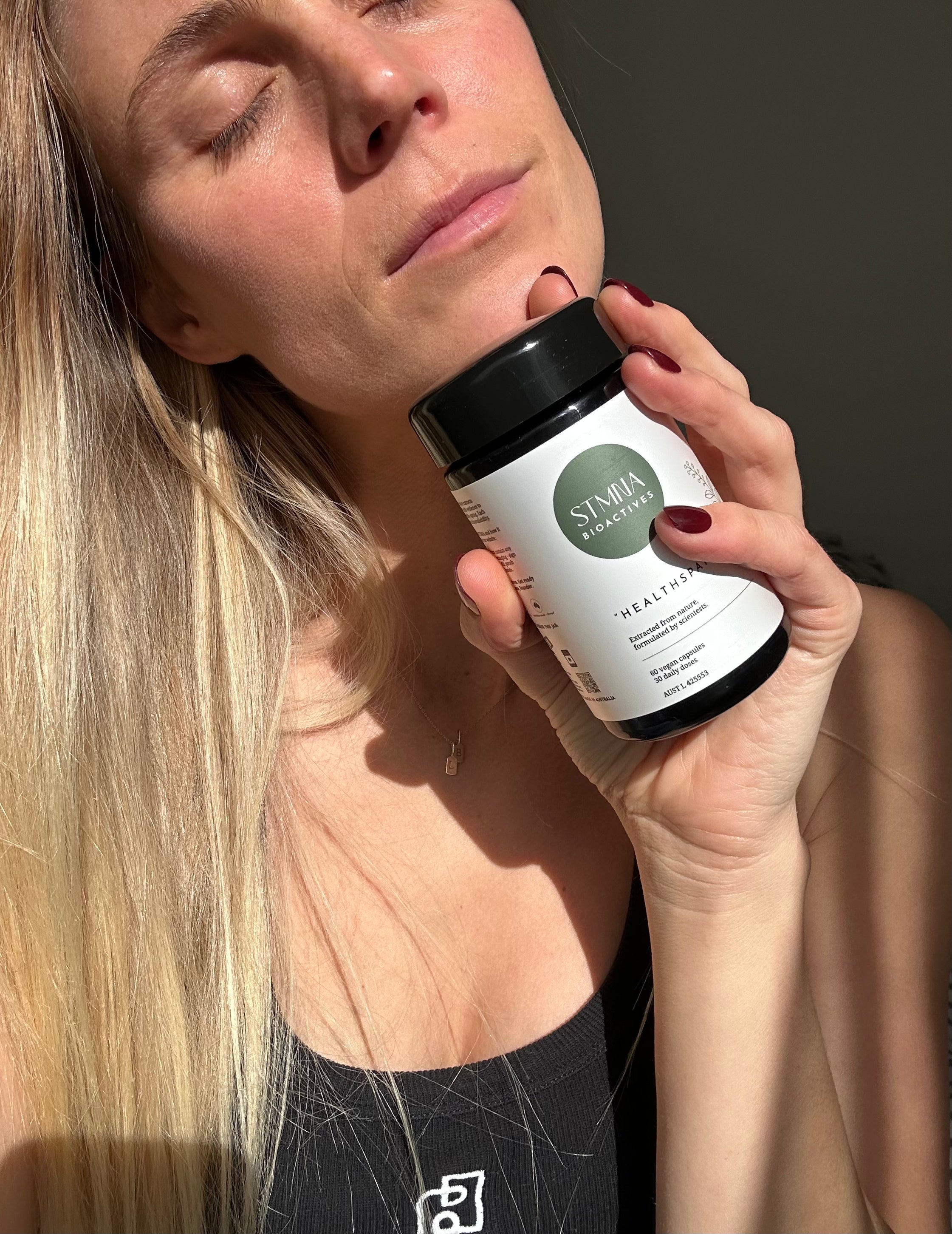 Person holding a supplement bottle labeled 'STMNA' against a neutral background